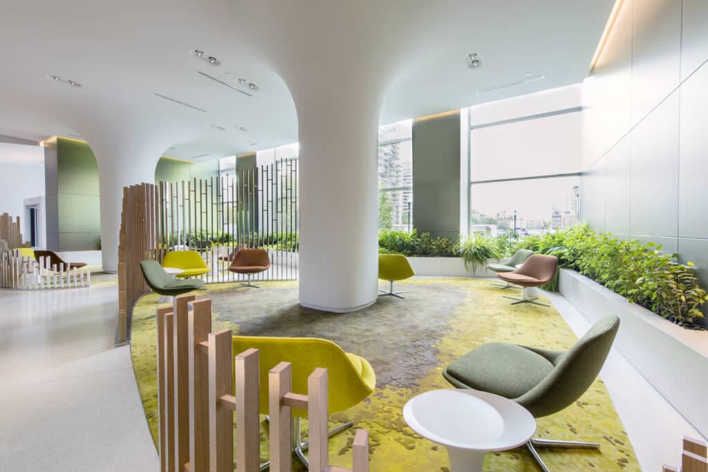 An open, bright, and green lobby space with floor to ceiling windows and plants