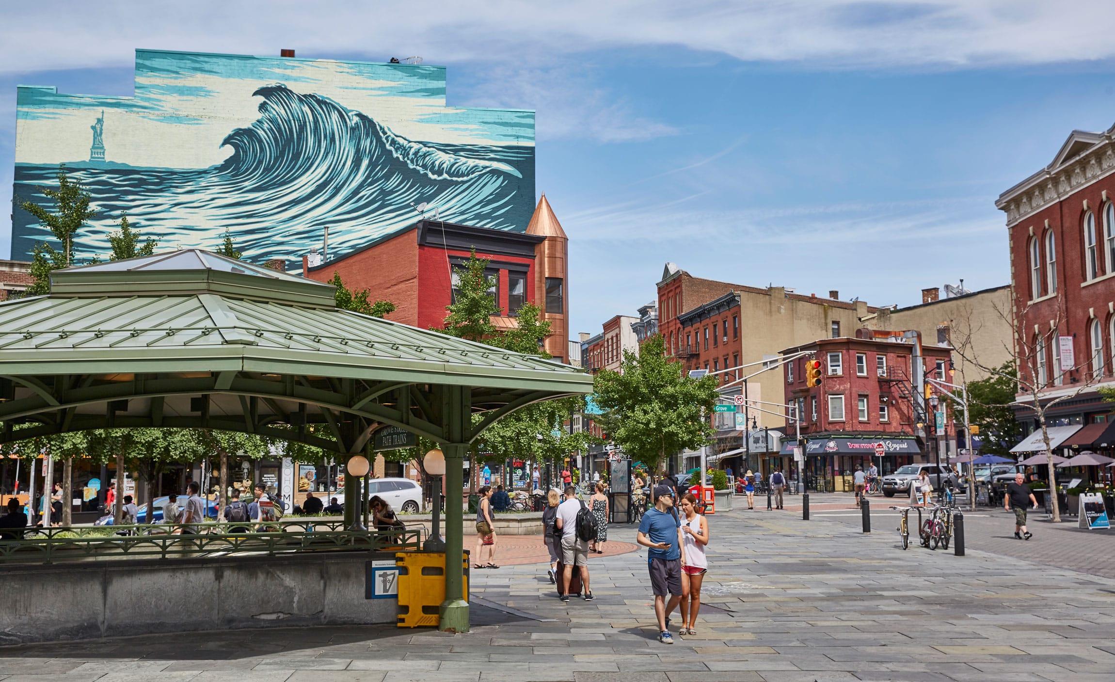 Pedestrians walking along the street with a mural of a large wave in the back