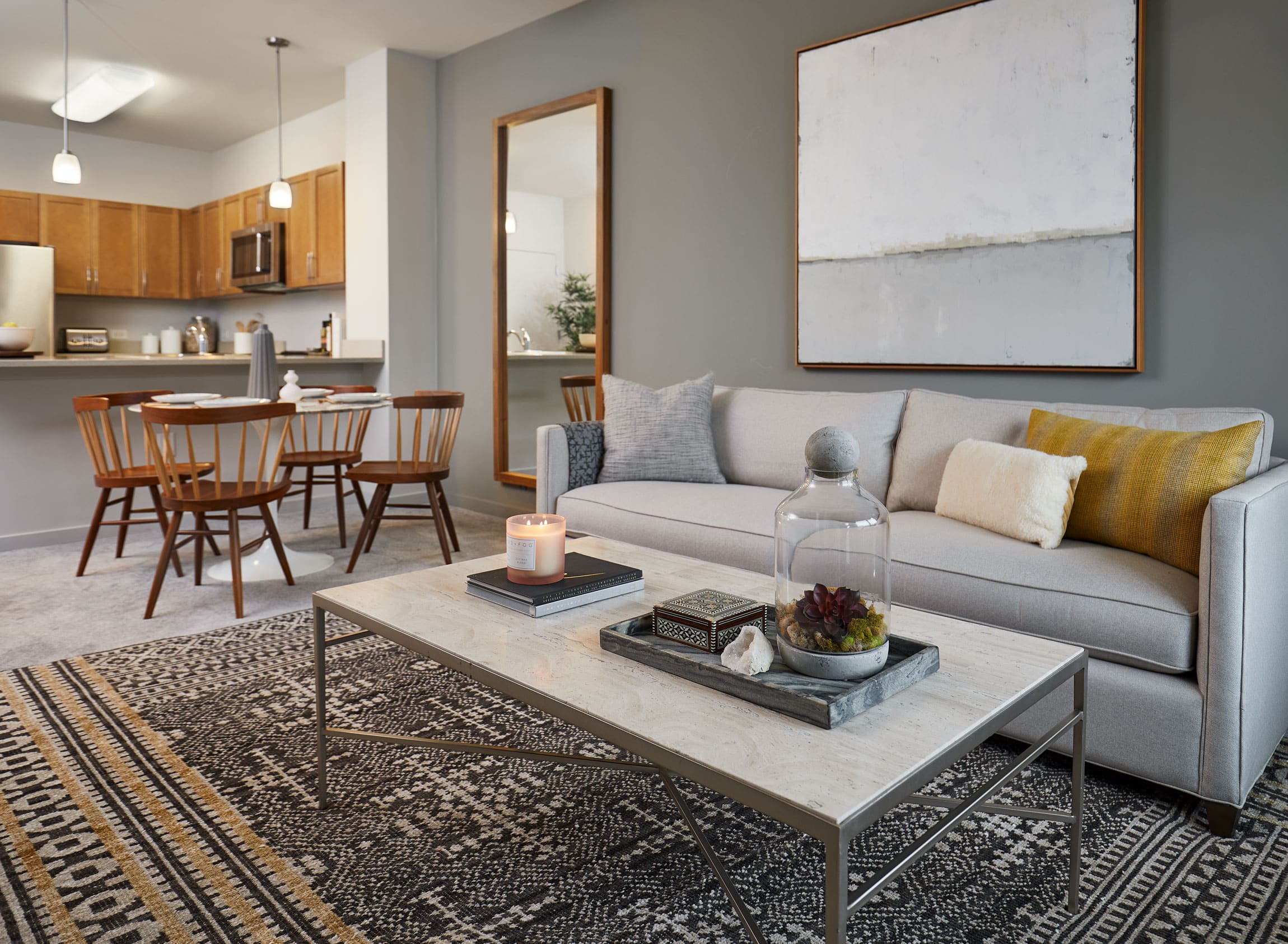 apartment interior with gray couch and coffee table, brown dining table and chairs and kitchen in the background